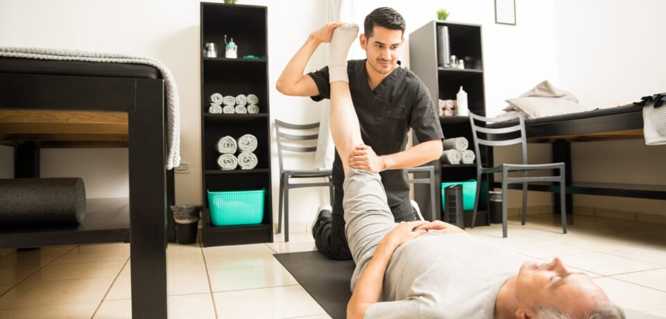 Physiotherapy doctor assisting elderly patient with leg exercise in clinic