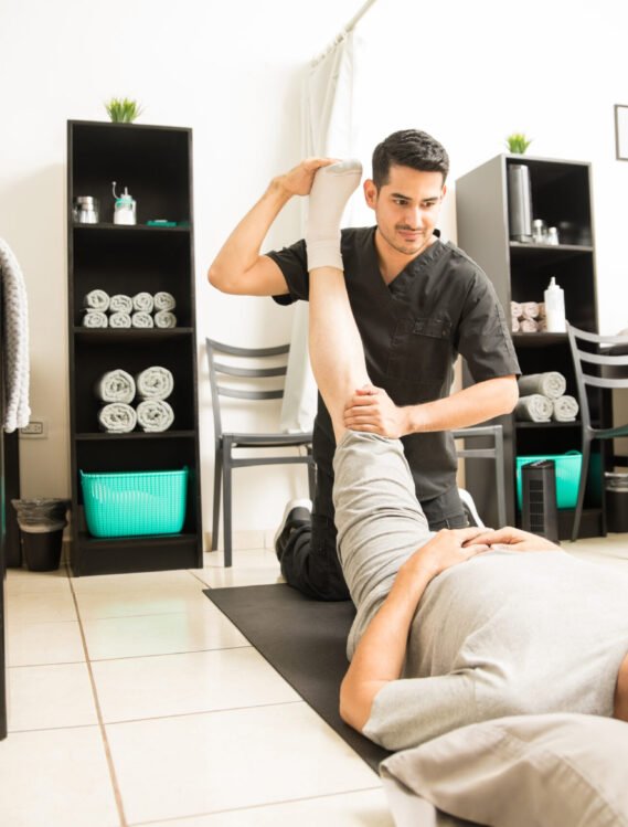 Physiotherapy doctor assisting elderly patient with leg exercise in clinic